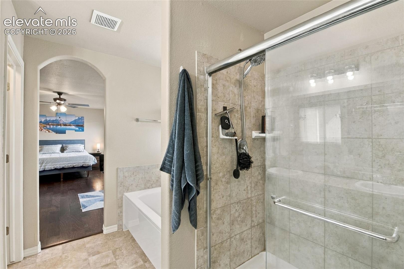 Bathroom featuring a glass-enclosed shower with tiled surround, separate soaking tub, and neutral floor tile
