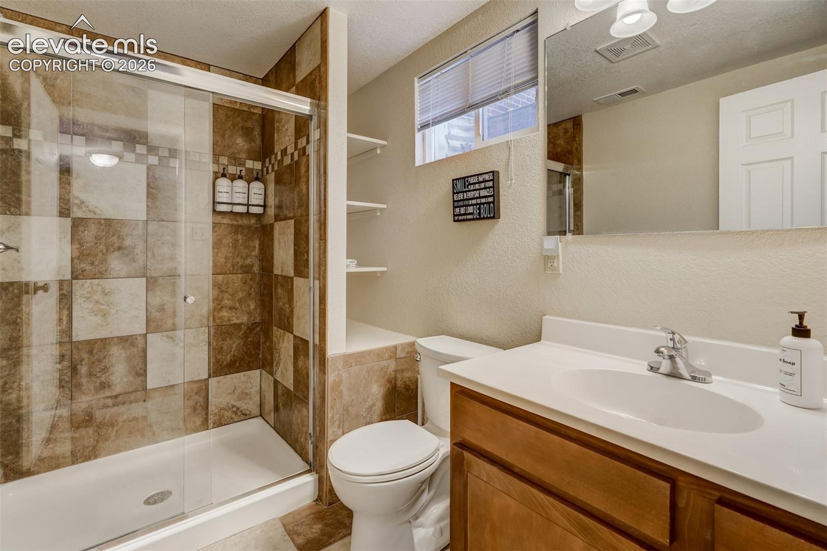 Bathroom featuring a glass-enclosed shower with tile surround, a single-sink vanity with wood-finish cabinetry, a toilet, and built-in shelving