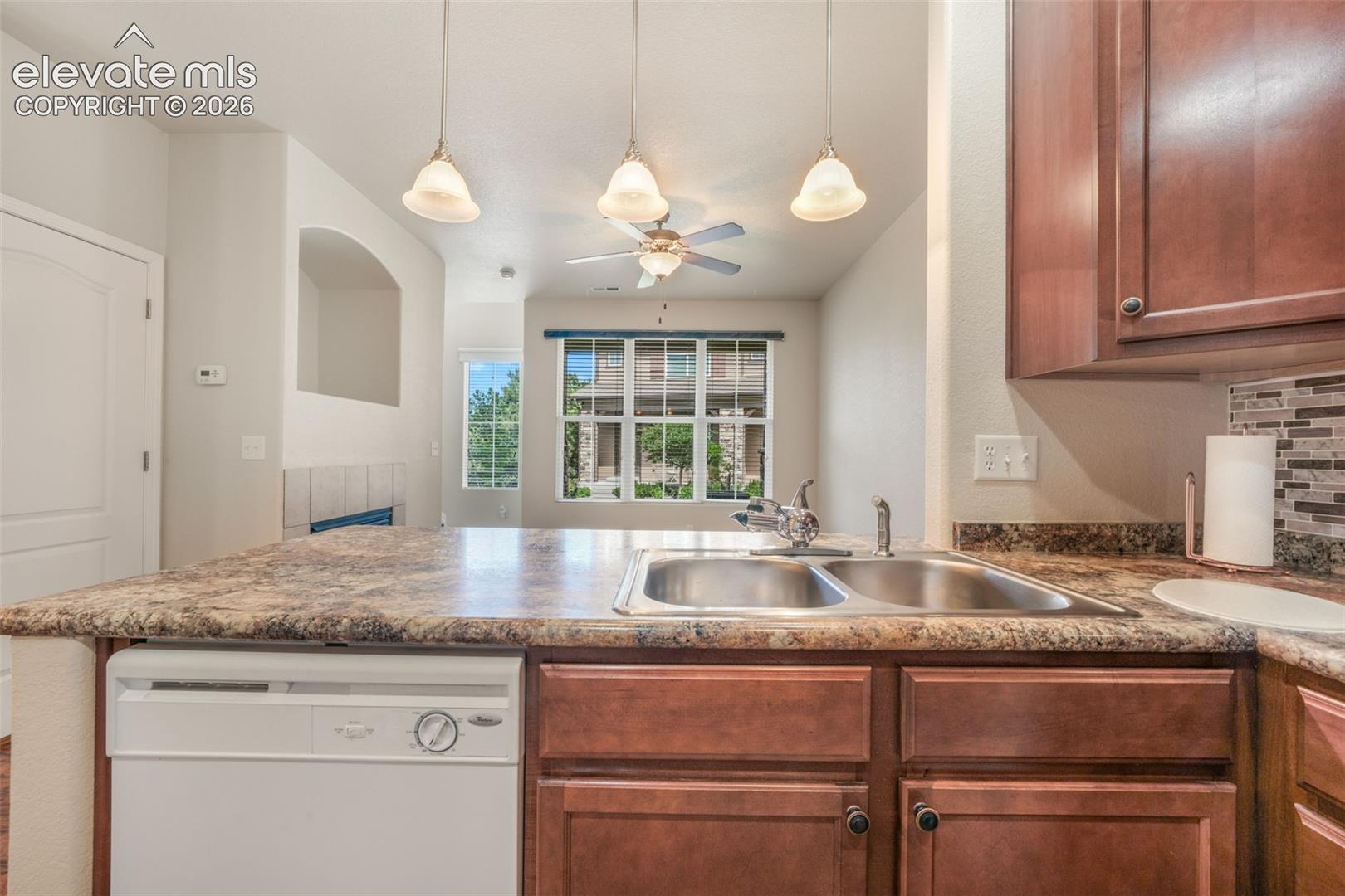 Kitchen featuring a double basin sink, dark wood-finish cabinetry, a patterned tile backsplash, and a built-in dishwasher