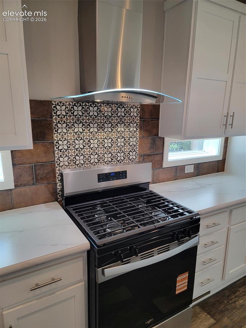 Kitchen featuring shaker-style cabinetry, stainless steel gas range, glass-canopy range hood, patterned tile backsplash, and quartz countertops