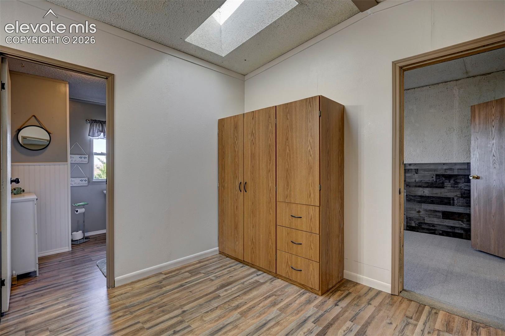 Bedroom featuring light wood-style floors, a skylight, a textured ceiling, wainscoting, and ornamental molding