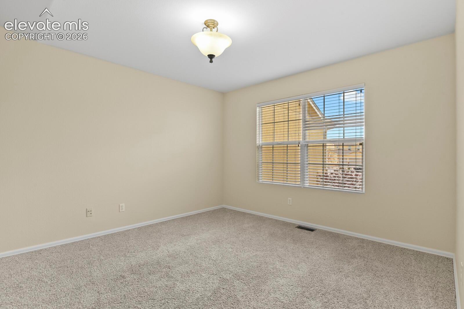 Inviting room featuring a large window with blinds, neutral-toned walls, plush carpet flooring, a ceiling-mounted light fixture, and white baseboards