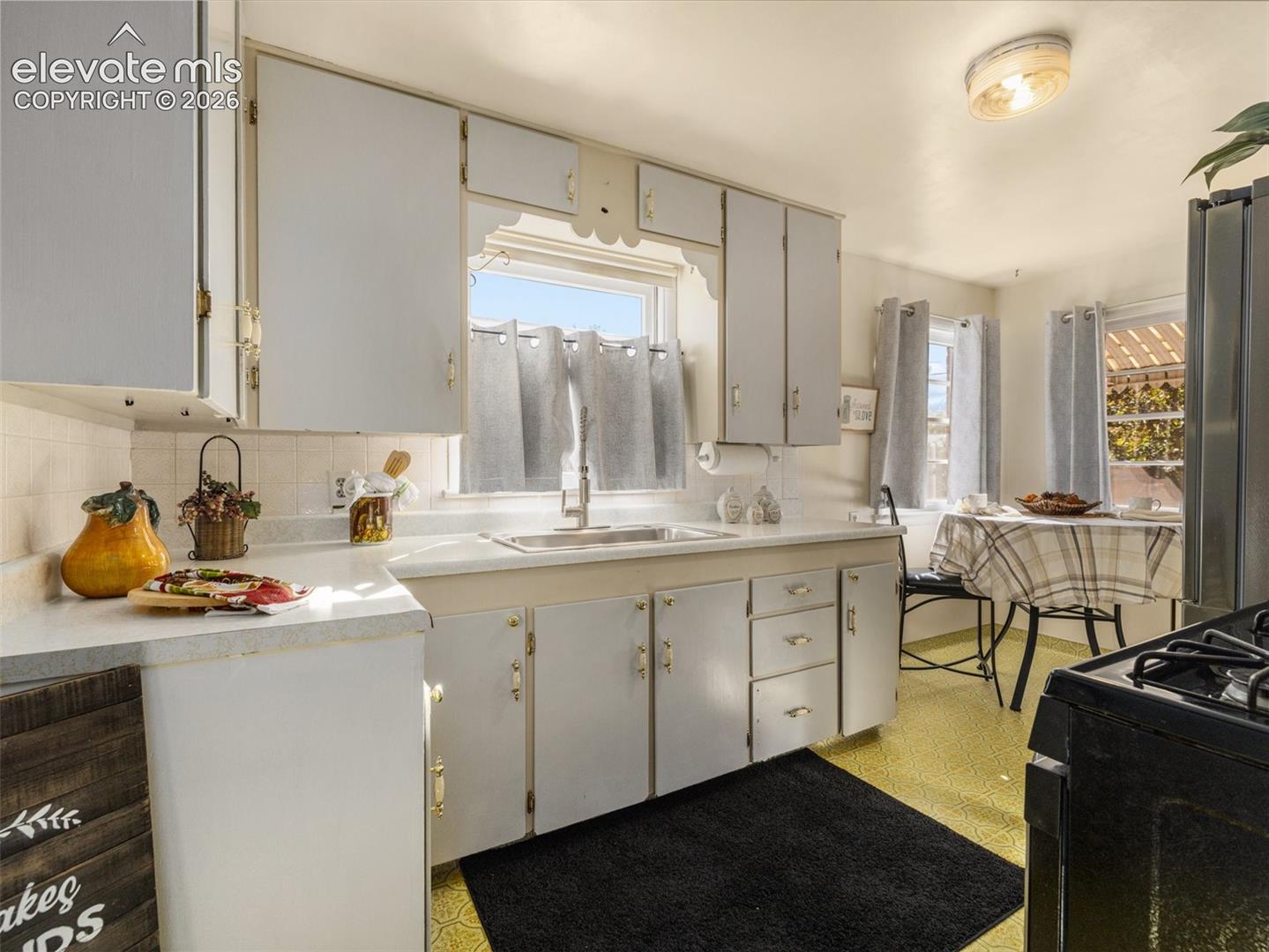Kitchen featuring white cabinetry, solid-surface countertops, a stainless steel undermount sink with a gooseneck faucet, and tiled backsplash
