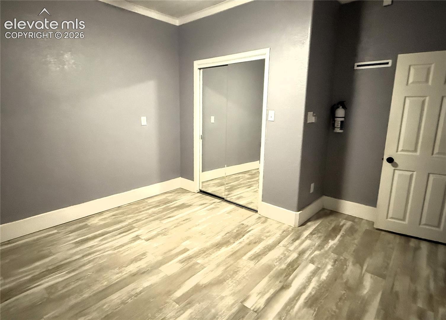 Room featuring wood-finish flooring, mirrored sliding closet doors, crown molding, and a six-panel interior door