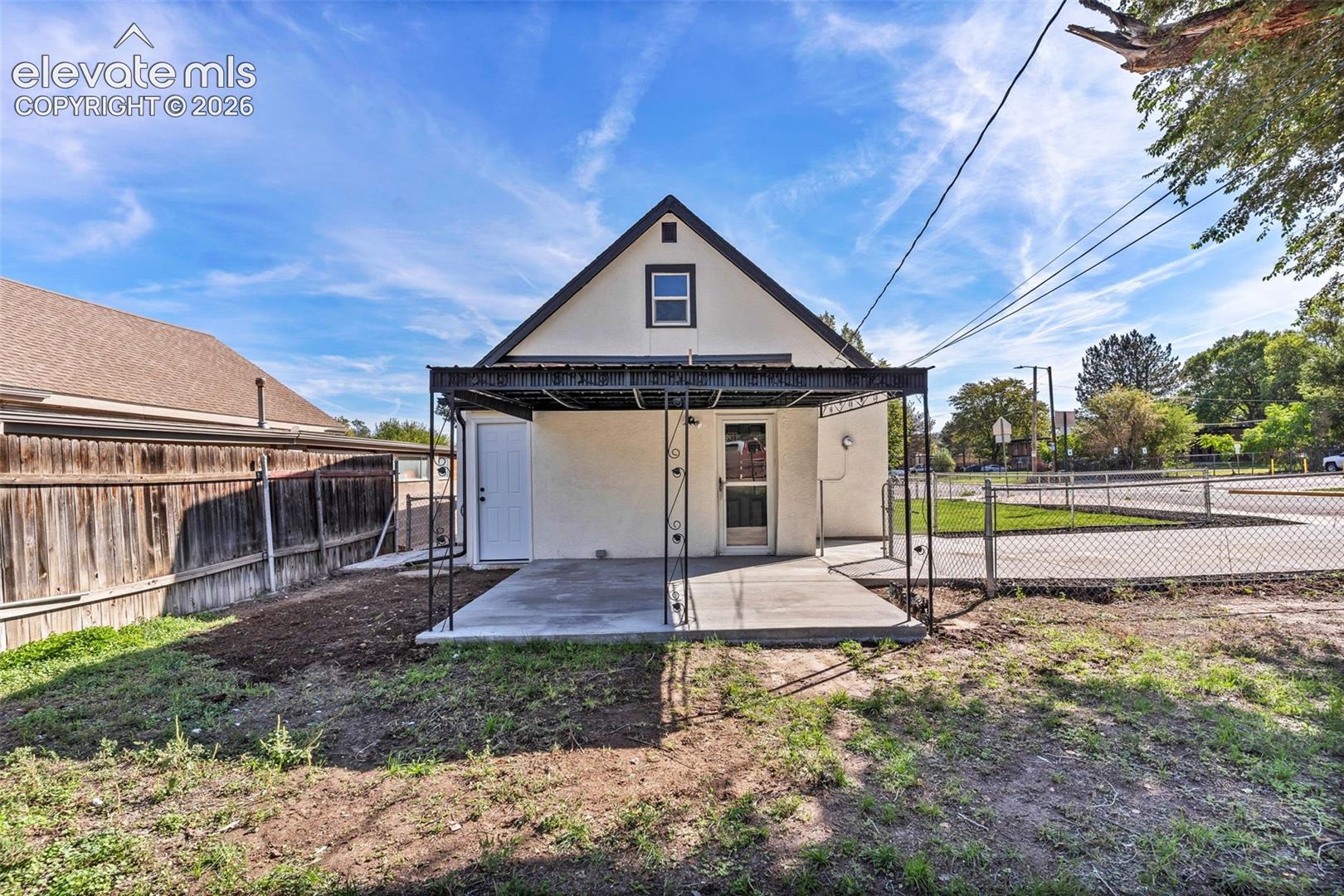 Stucco exterior featuring a covered concrete patio, metal-frame pergola, and perimeter wood fencing