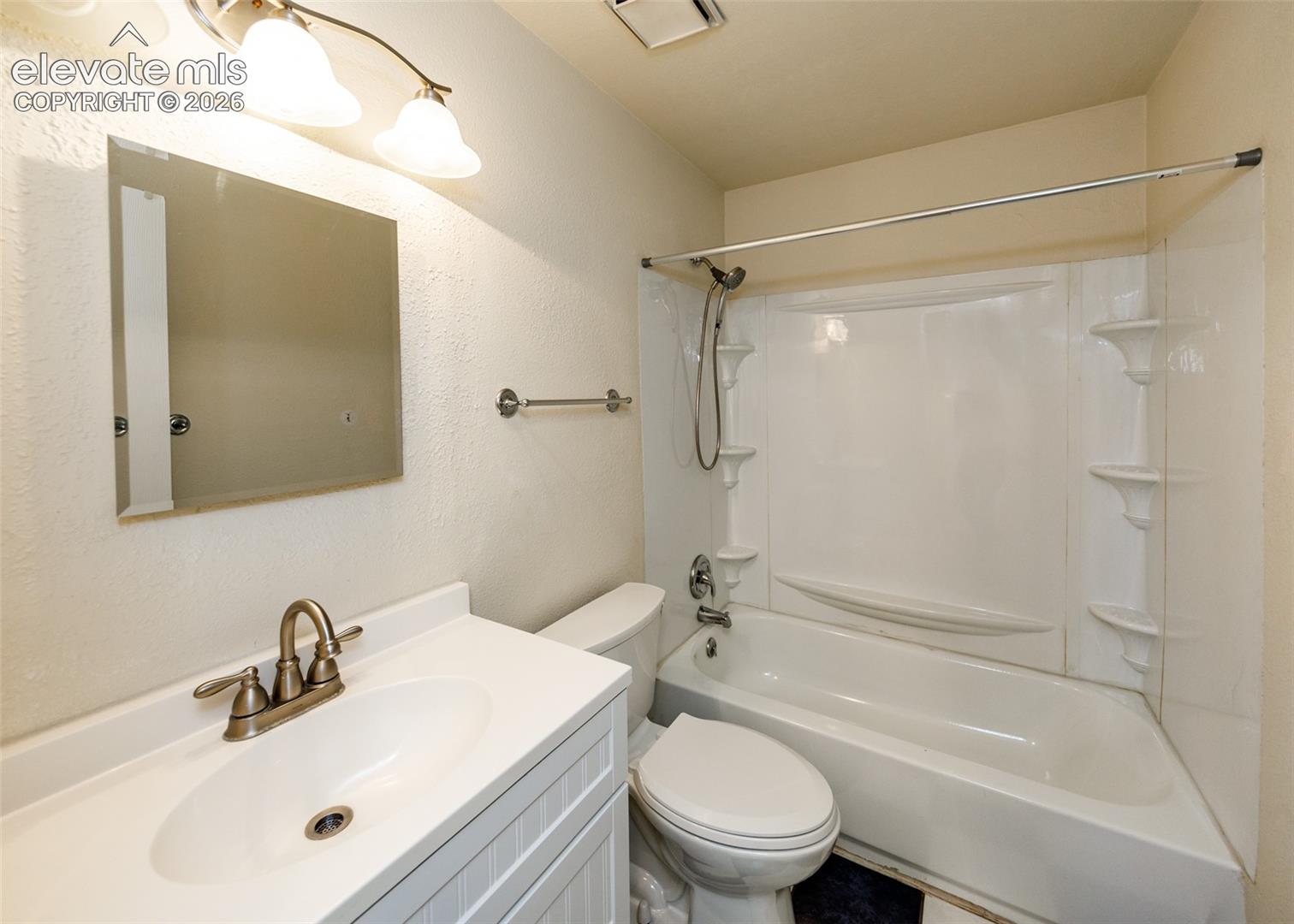 Bathroom featuring a white vanity with an integrated sink, dual-handle metal faucet, wall-mounted light fixture, and a tub-shower combination with an adjustable handheld sprayer