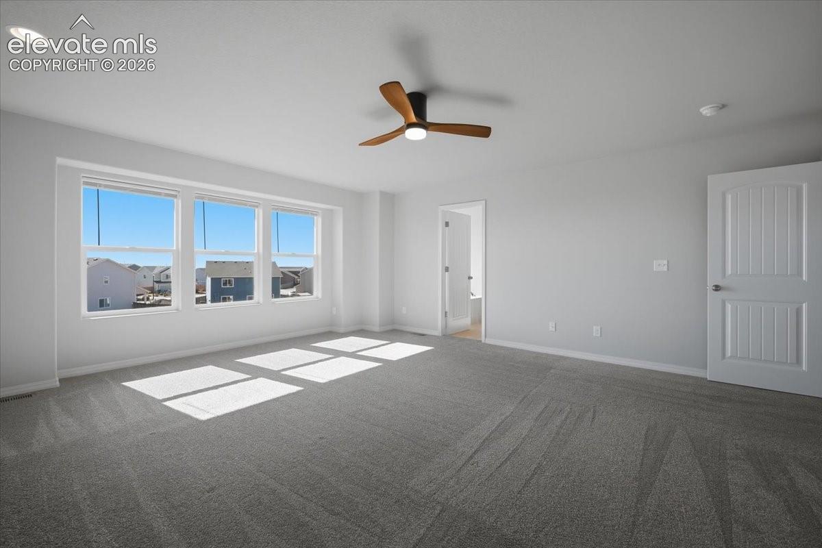Room featuring wall-to-wall carpeting, three windows with exterior exposure, a ceiling-mounted fan with integrated lighting, and a multi-panel interior door