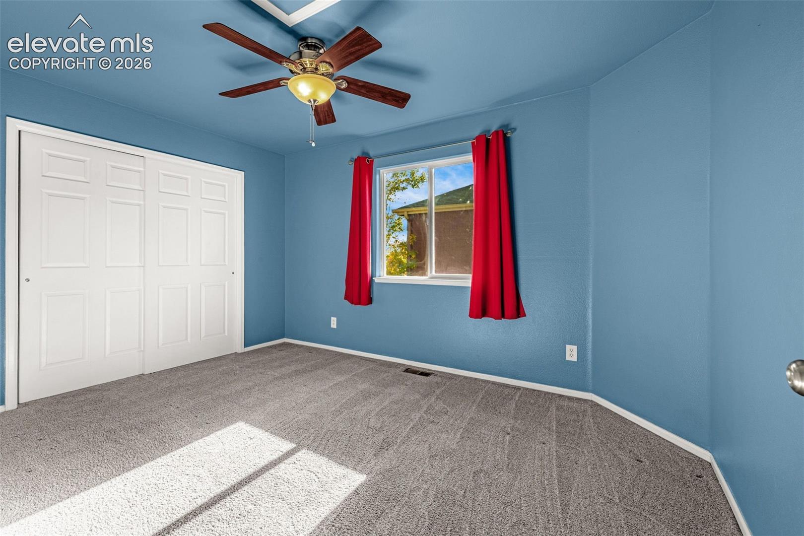 Bedroom featuring wall-to-wall carpeting, dual-panel sliding closet doors, and a ceiling fan with integrated lighting