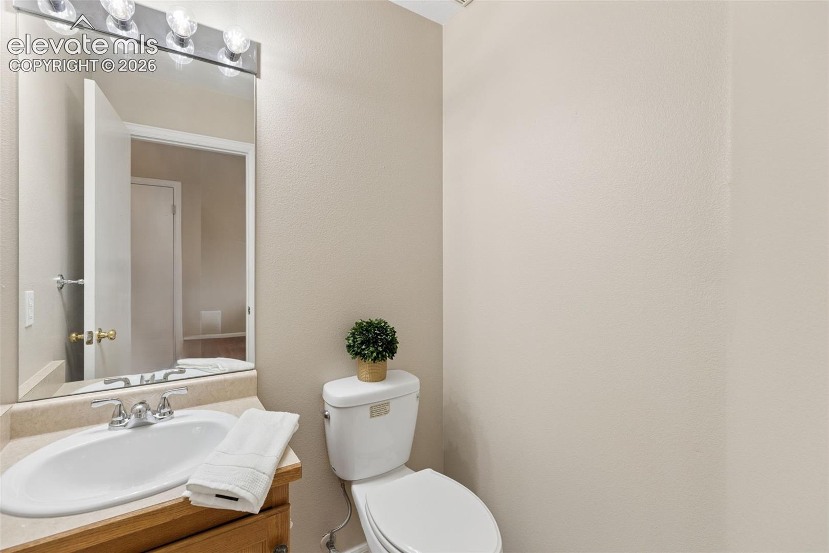 Built-in vanity with a stone-finish countertop, undermount oval sink, polished chrome faucet, wall-mounted mirror, and multi-bulb light fixture