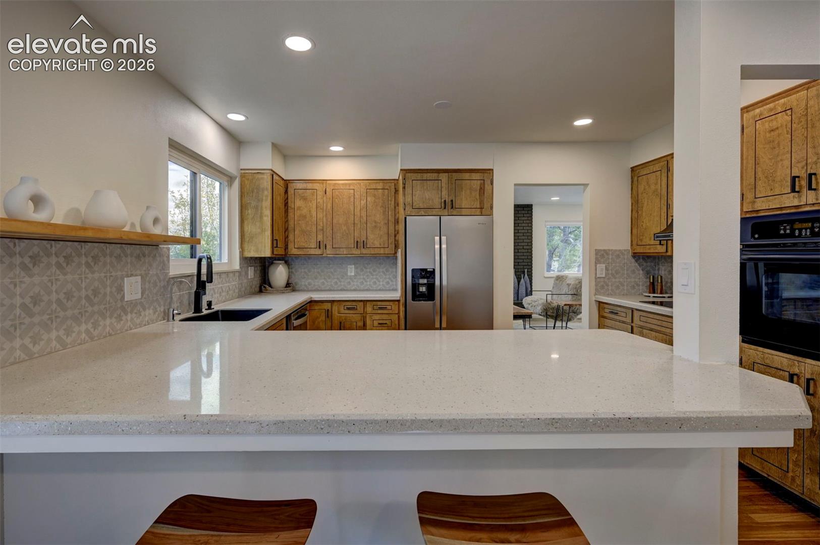 Kitchen featuring a wrap-around stone countertop, wood cabinetry, patterned tile backsplash, recessed lighting, and a built-in oven