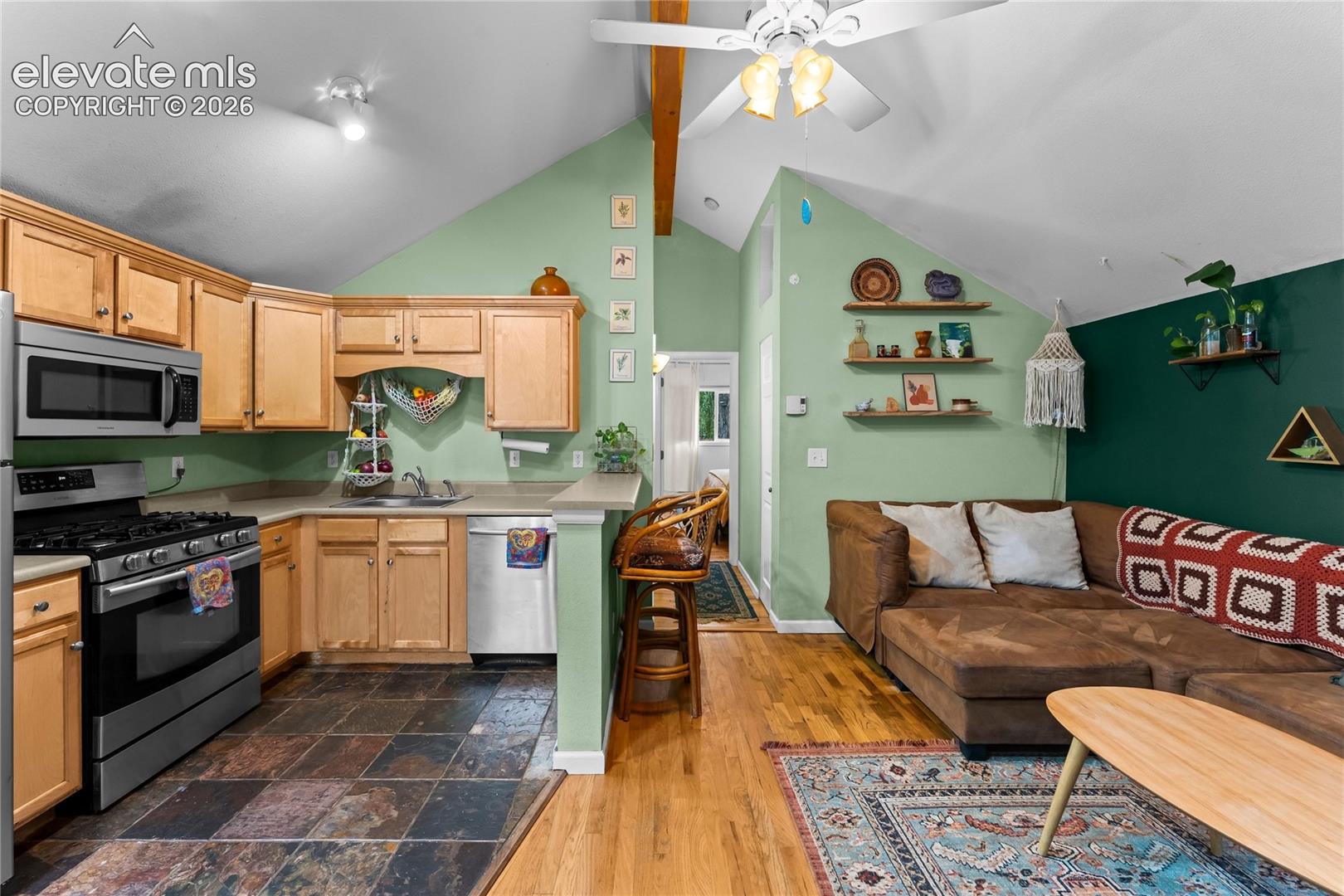 Kitchen featuring light-finish cabinetry, stainless steel appliances, slate-tile flooring, vaulted ceilings, and wood-finish flooring