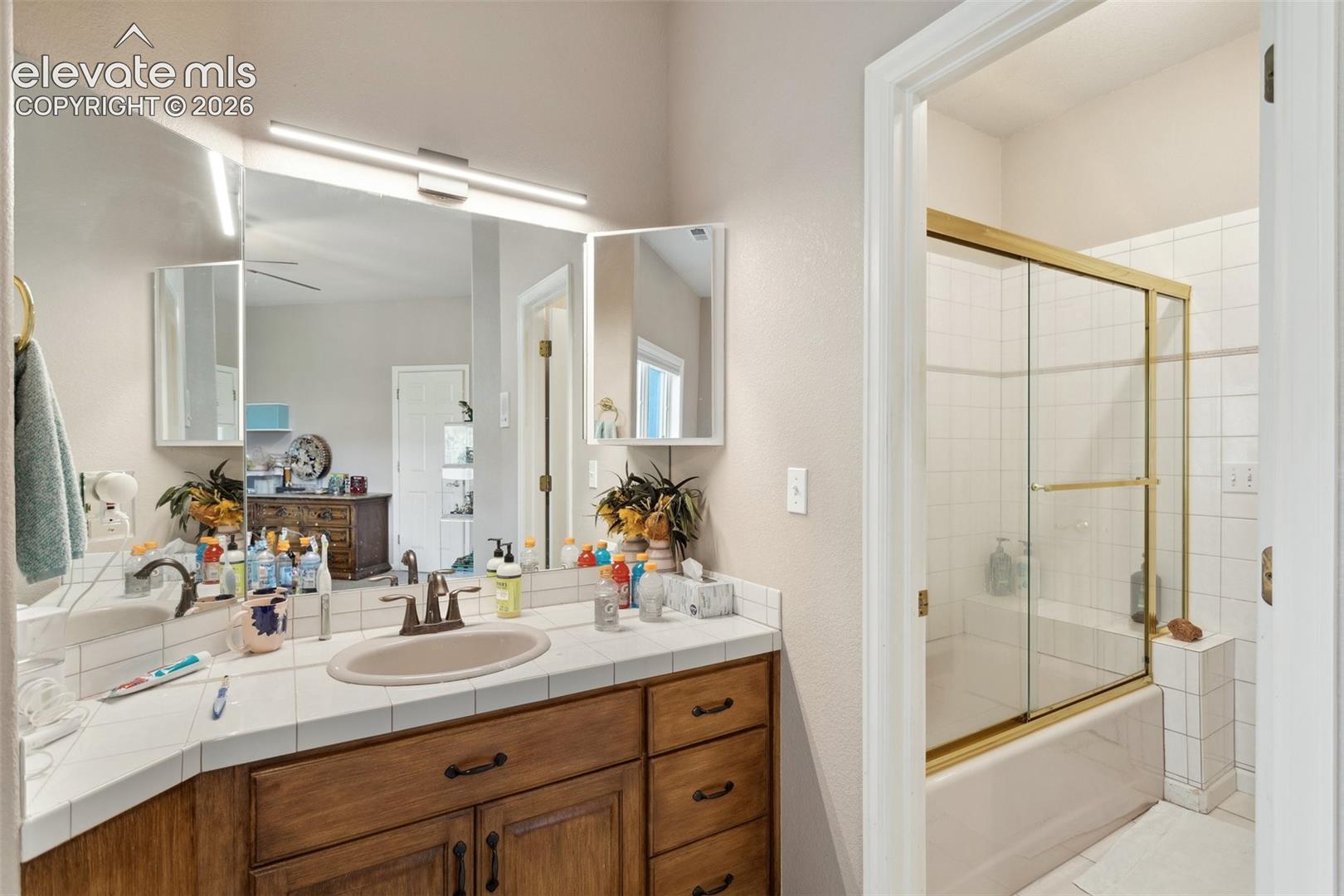 Bathroom vanity featuring a single basin, tile countertop, and wood-finish cabinetry