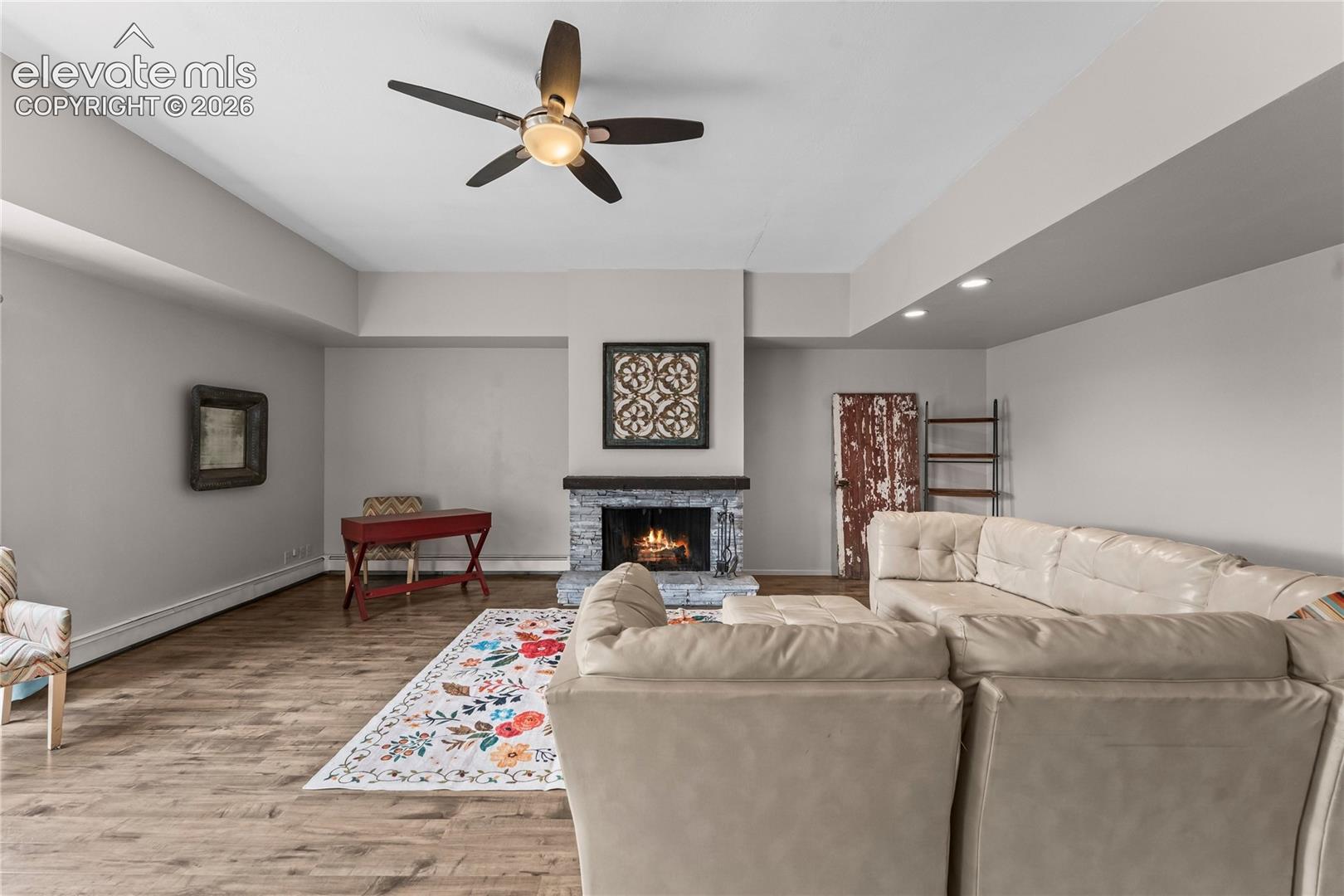 Fireplace with stone-style surround and wood mantel, wood-finish flooring, recessed lighting, and a multi-blade ceiling fan