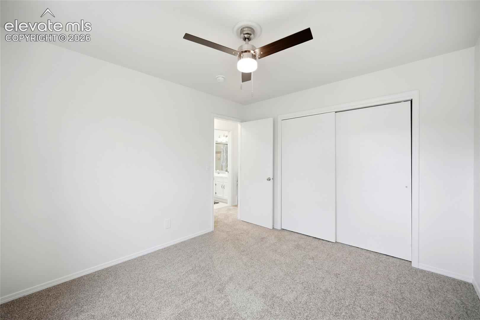 Neutral-toned carpeting, ceiling fan with integrated lighting, and dual-panel sliding closet doors