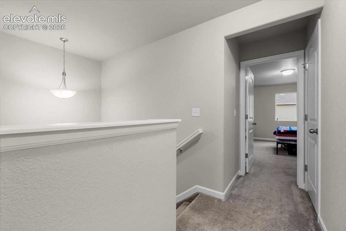 Upper-level landing with carpet flooring, pendant lighting, and neutral wall paint