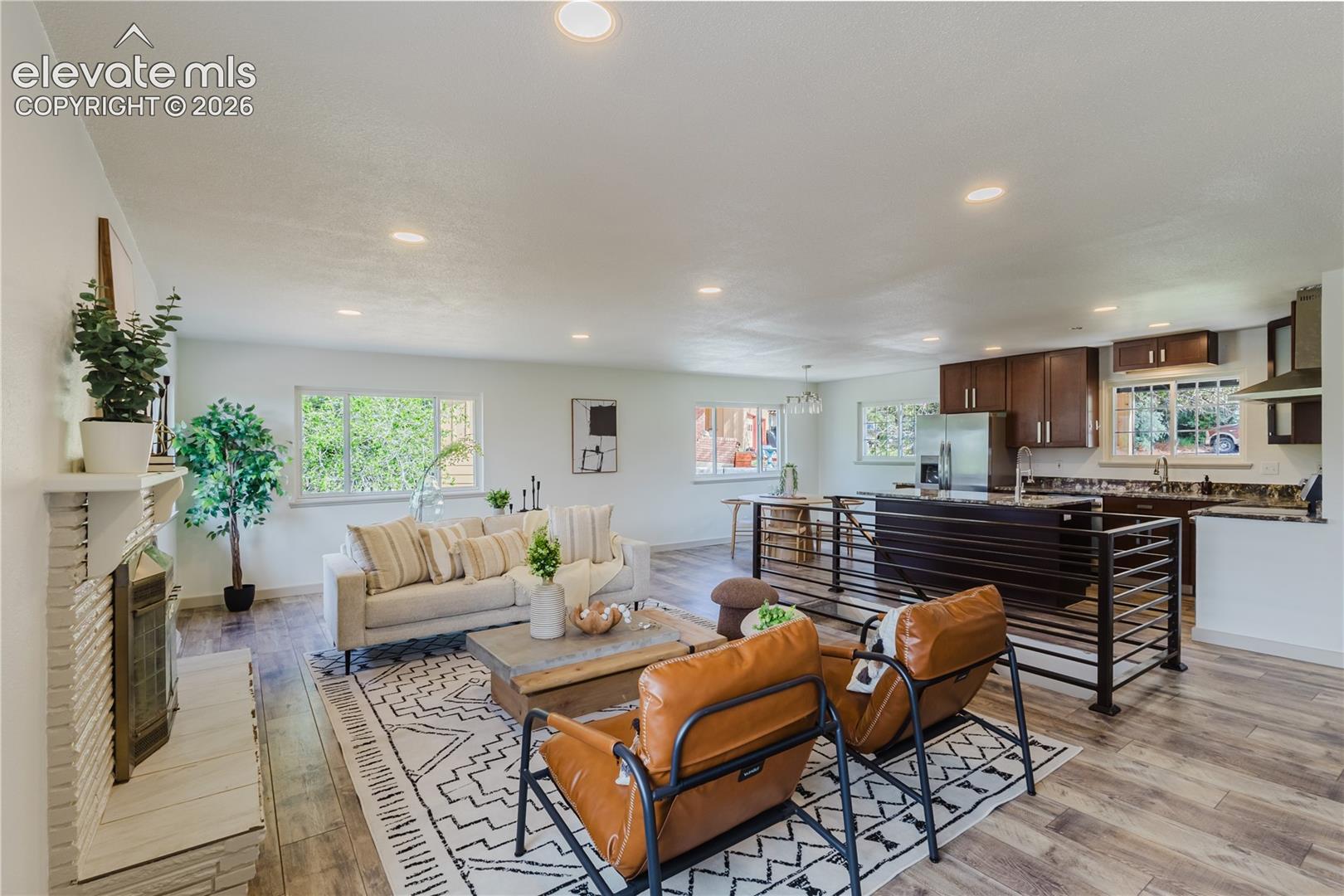 Open-concept living space featuring wood-finish flooring, recessed lighting, and a white brick fireplace