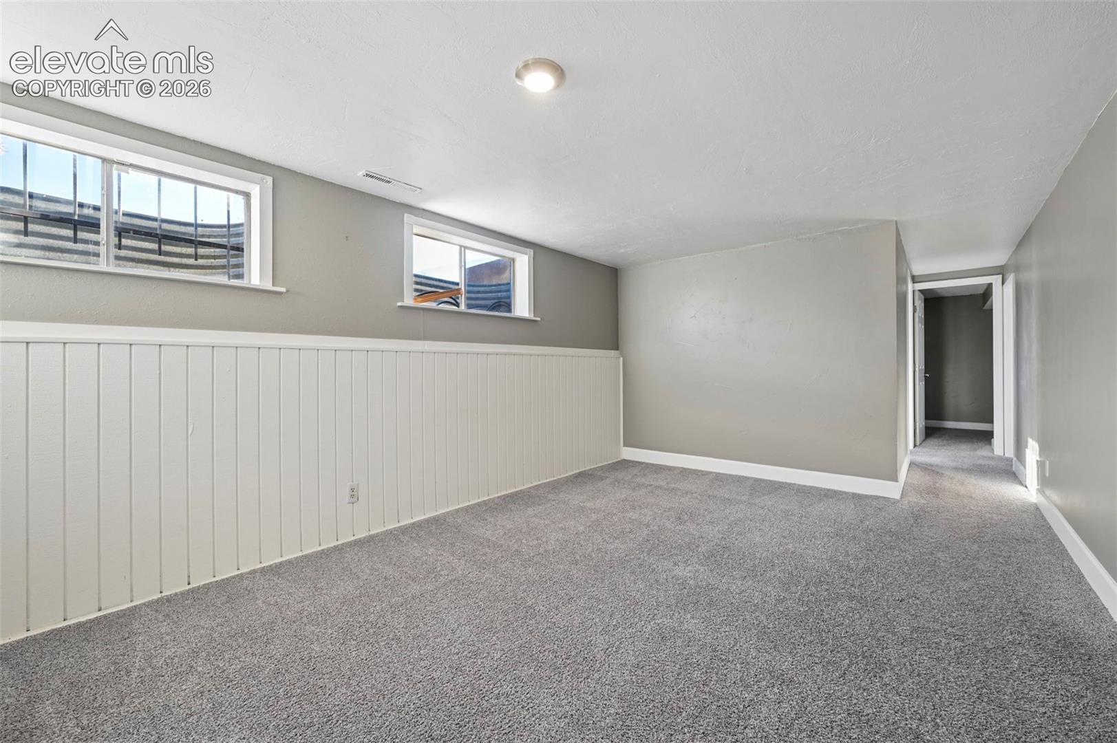 Neutral-toned interior space featuring white beadboard wainscoting, neutral carpeting, and sliding windows set within window wells