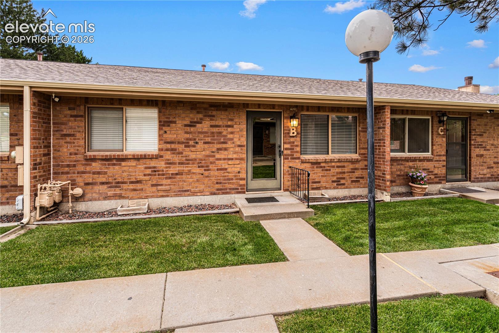 Single-story brick exterior with asphalt shingle roofing, concrete walkways, and metallic-framed glass storm doors