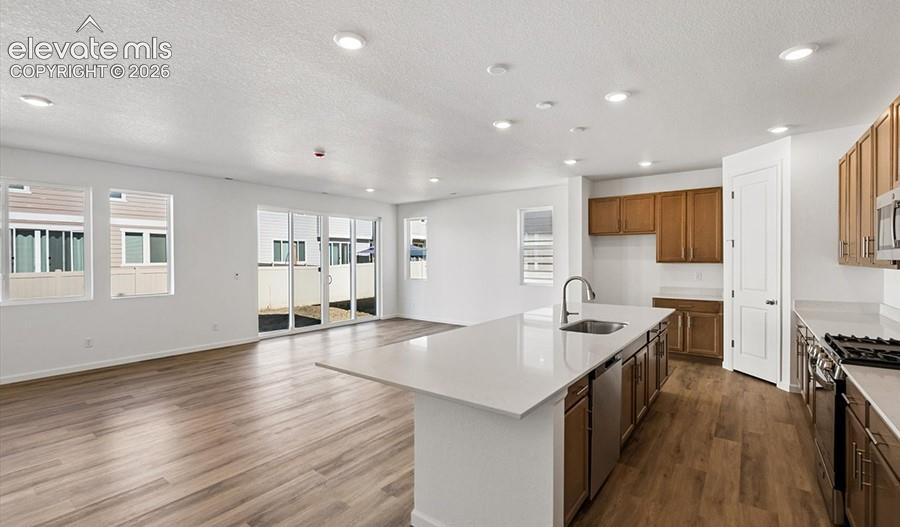 Open-concept kitchen featuring an island with quartz countertop, wood-finish cabinetry, stainless steel appliances, recessed lighting, and wood-finish flooring
