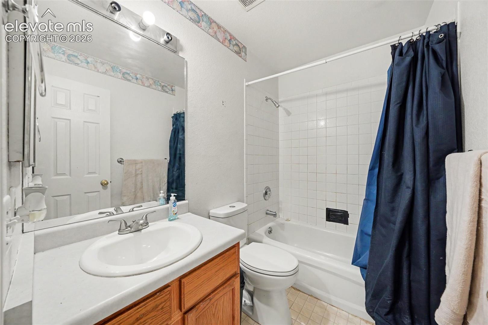 Bathroom featuring a wood-finish vanity with a drop-in sink, expansive wall-mounted mirror, lighting fixture, and a tile-surround shower and tub combination
