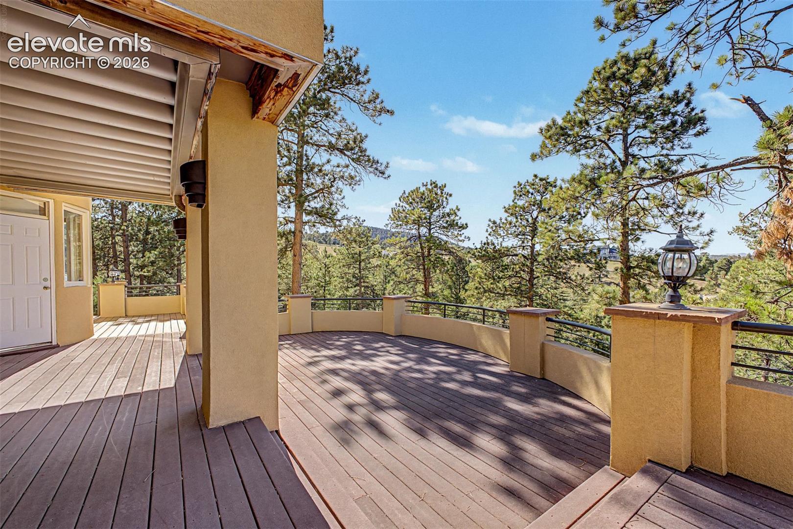 Expansive outdoor decking featuring a curved railing, stucco exterior, and a built-in pillar light fixture