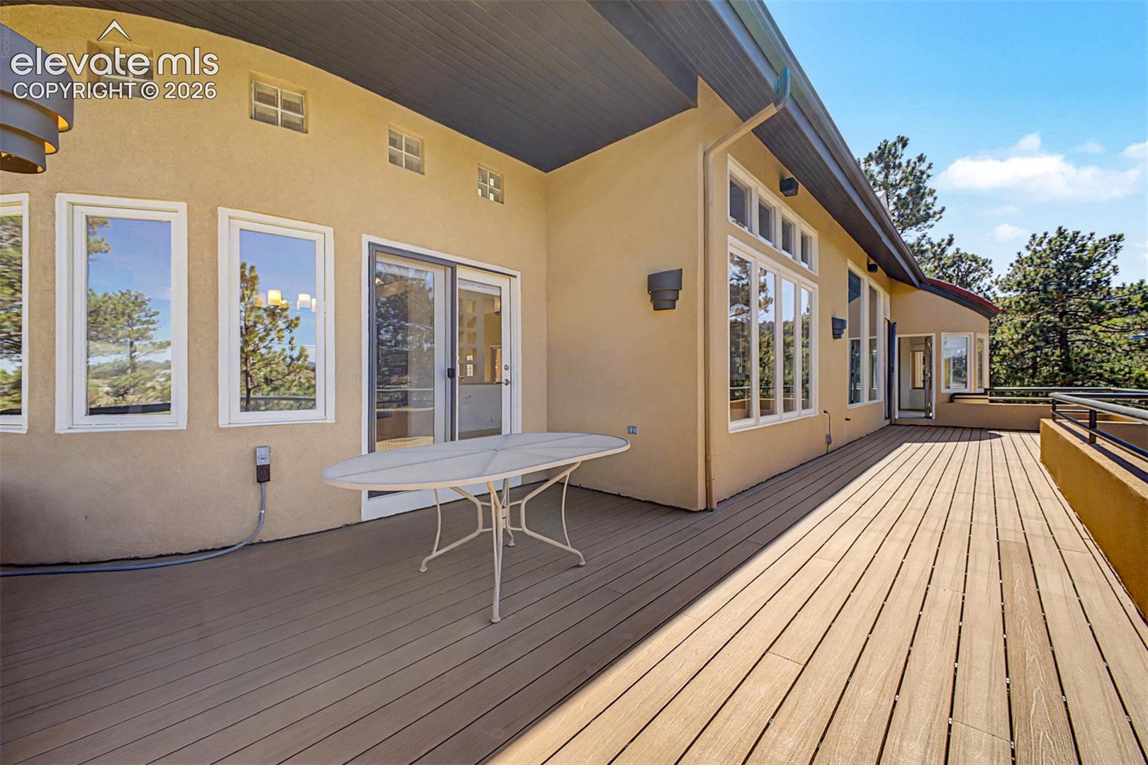 Expansive outdoor deck featuring wood-finish flooring, stucco exterior, multiple large windows, and a glass sliding door