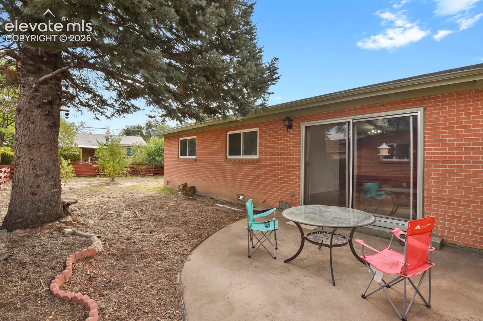 Red brick exterior featuring a concrete patio, sliding glass door, and large mature trees