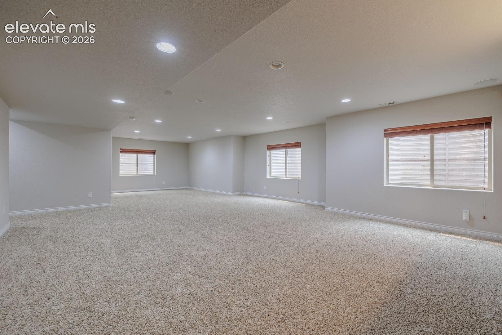 Expansive carpeted room featuring recessed lighting and multiple windows with wood-tone blinds