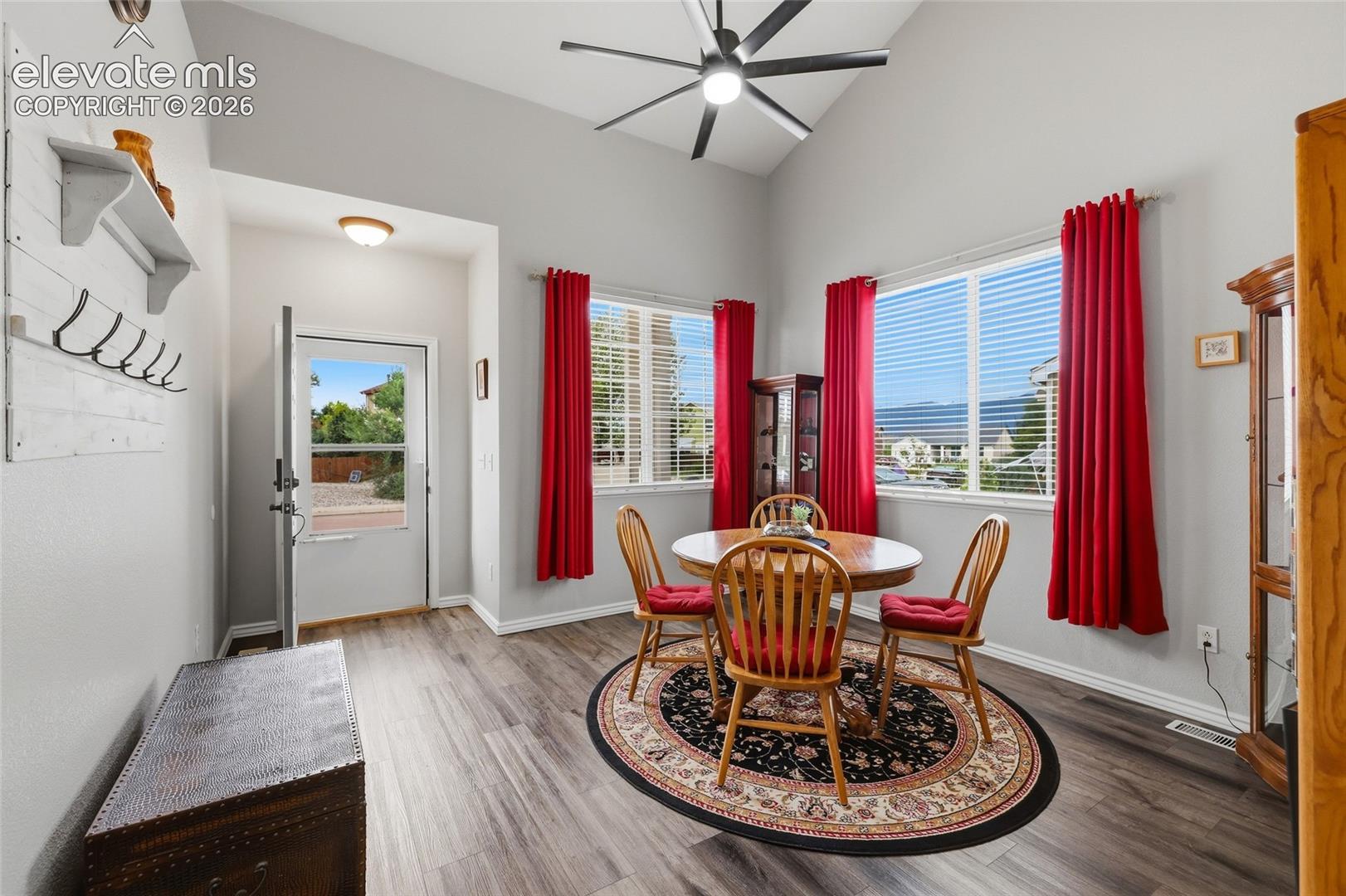 Vaulted ceiling with a ceiling fan, multiple windows with blinds, and wood-finish flooring