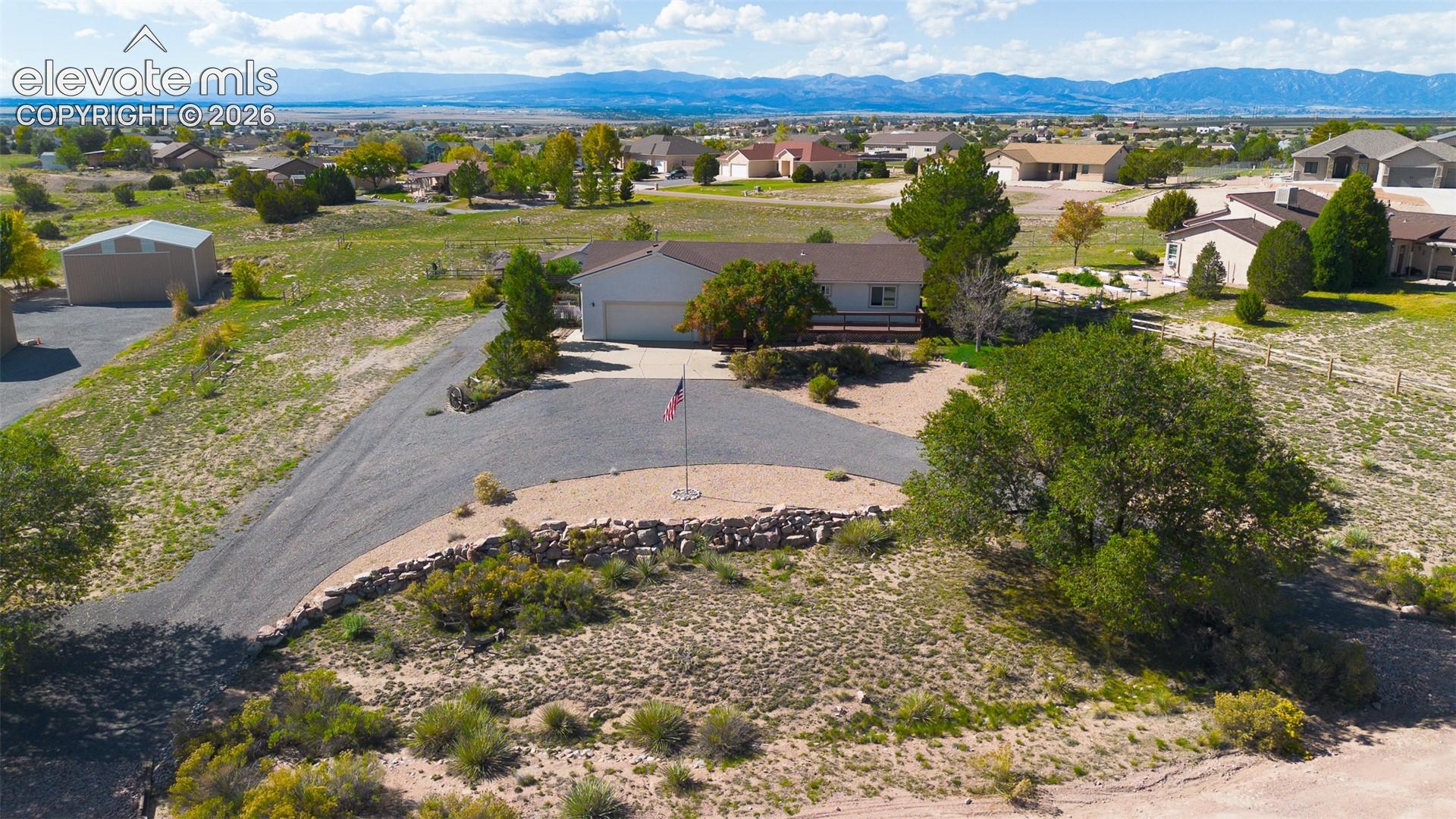 Single-level residence featuring a detached garage, expansive gravel driveway, stacked stone retaining wall, and mountain range backdrop