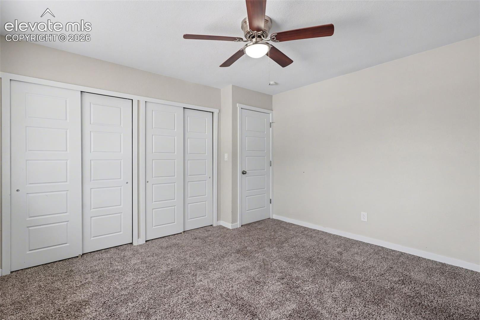 Room featuring neutral wall tones, textile flooring, a multi-blade ceiling fan with integrated light fixture, dual sliding closet doors, and a paneled interior door