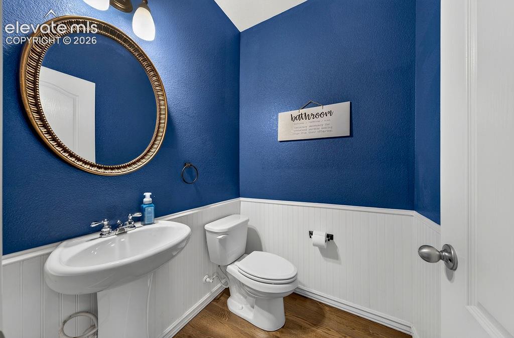 Pedestal sink with chrome fixtures, oval framed mirror, and wood-finish flooring, complemented by wainscoting