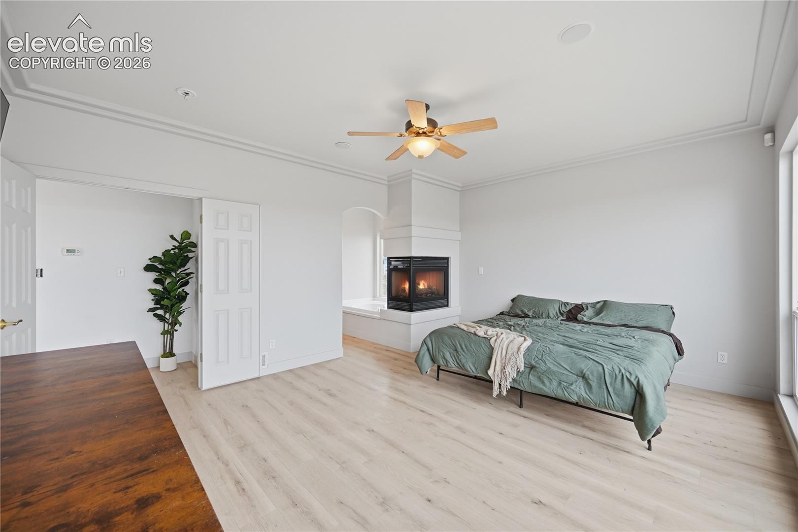 Light-toned wood-finish flooring, two-sided fireplace with a raised hearth, crown molding, and a ceiling fan with integrated lighting
