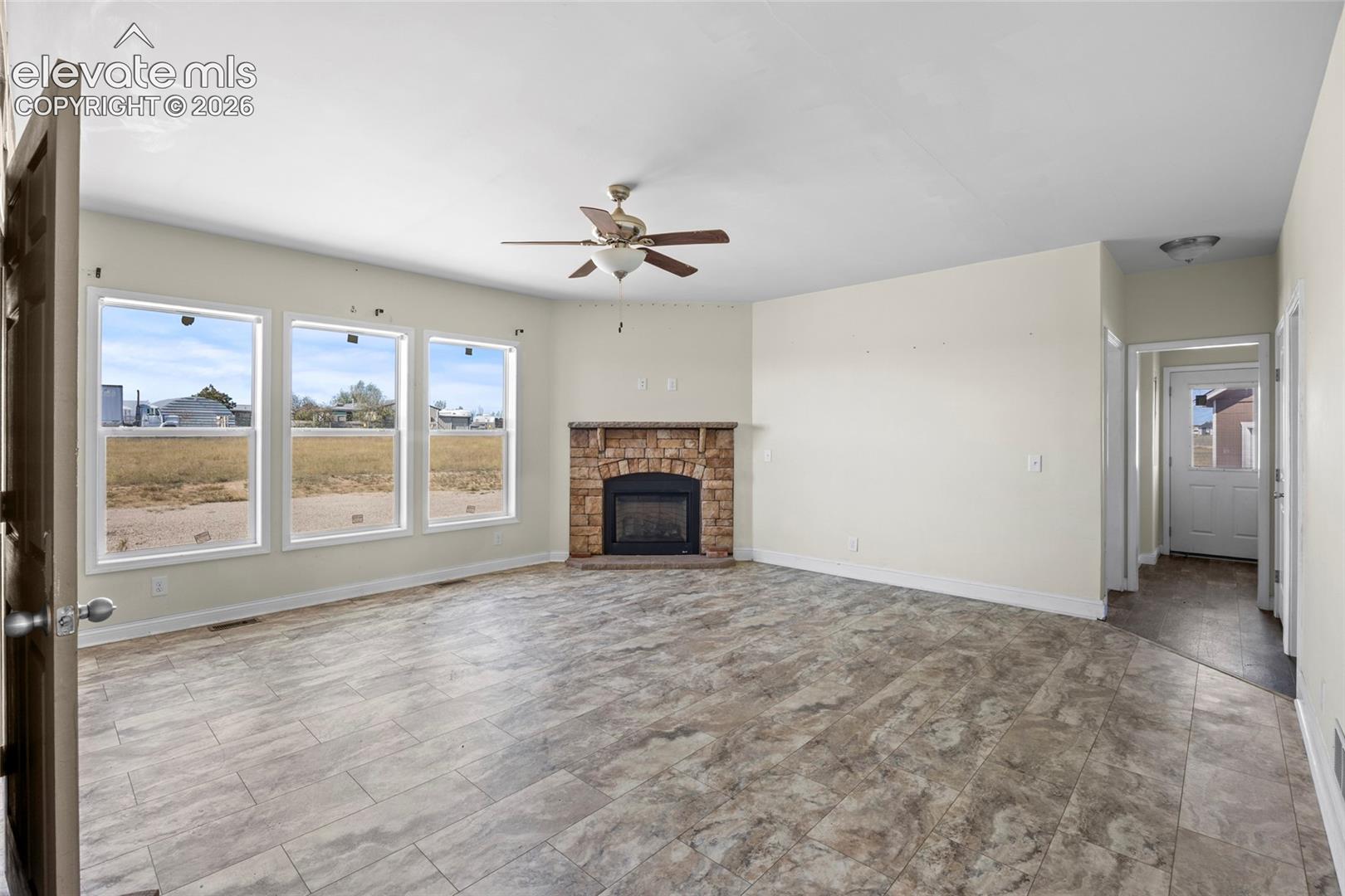 Tile flooring, stone-surround fireplace, triple pane windows, and ceiling fan