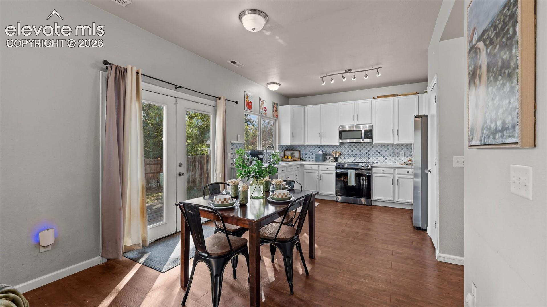 Open-concept kitchen with white cabinetry, stainless steel appliances, and wood-finish flooring