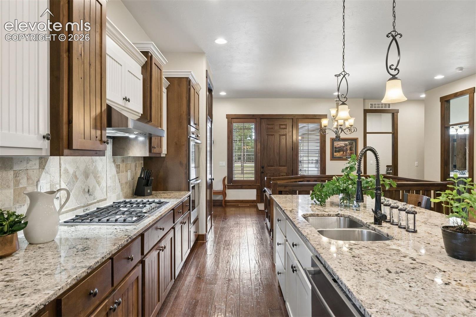 Kitchen featuring a spacious island with stone countertops, two-tone custom cabinetry, a built-in double oven, gas range, and wood-finish flooring