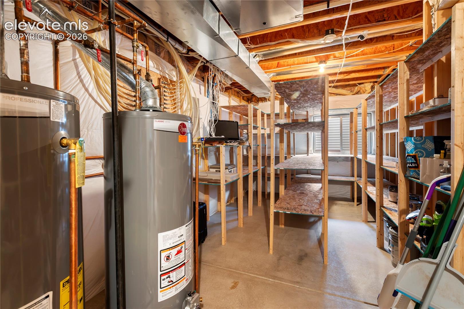 Dual water heaters, exposed wood joists, concrete flooring, and extensive built-in shelving