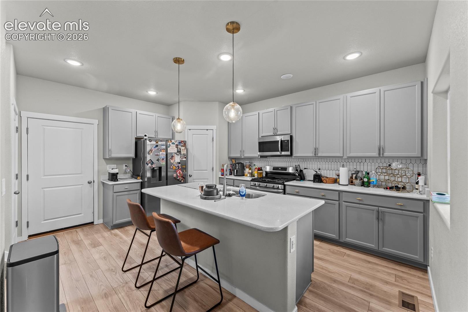 Kitchen featuring light wood-finish flooring, gray cabinetry, a central island with a white countertop, recessed lighting, and pendant fixtures