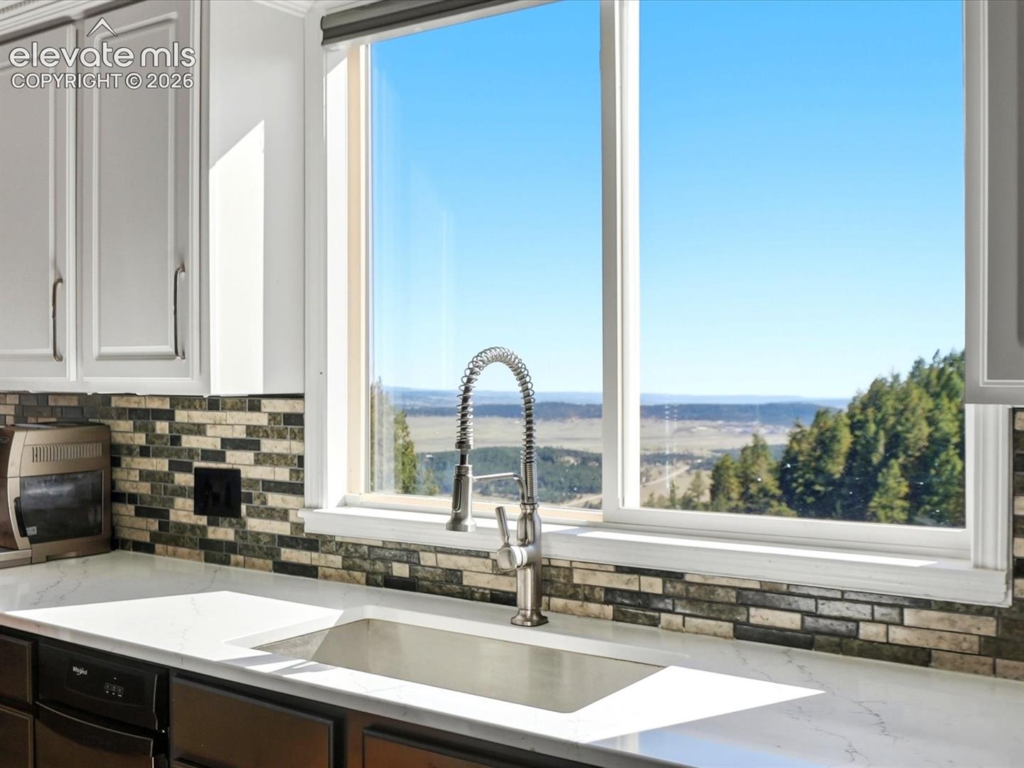 Kitchen featuring a white countertop with an integrated rectangular sink, industrial-style high-arc faucet, multi-toned stone mosaic backsplash, and crisp white cabinetry