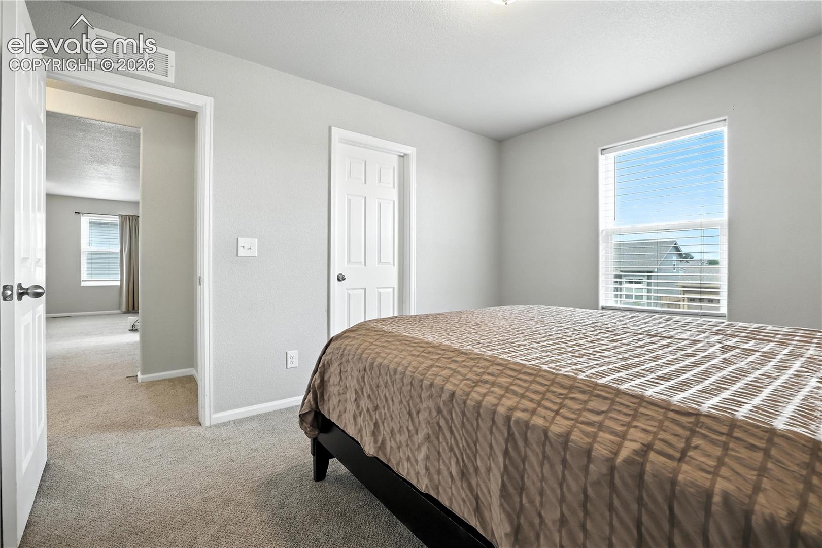 Neutral gray wall paint, white trim, carpet flooring, window with blinds, and white interior doors