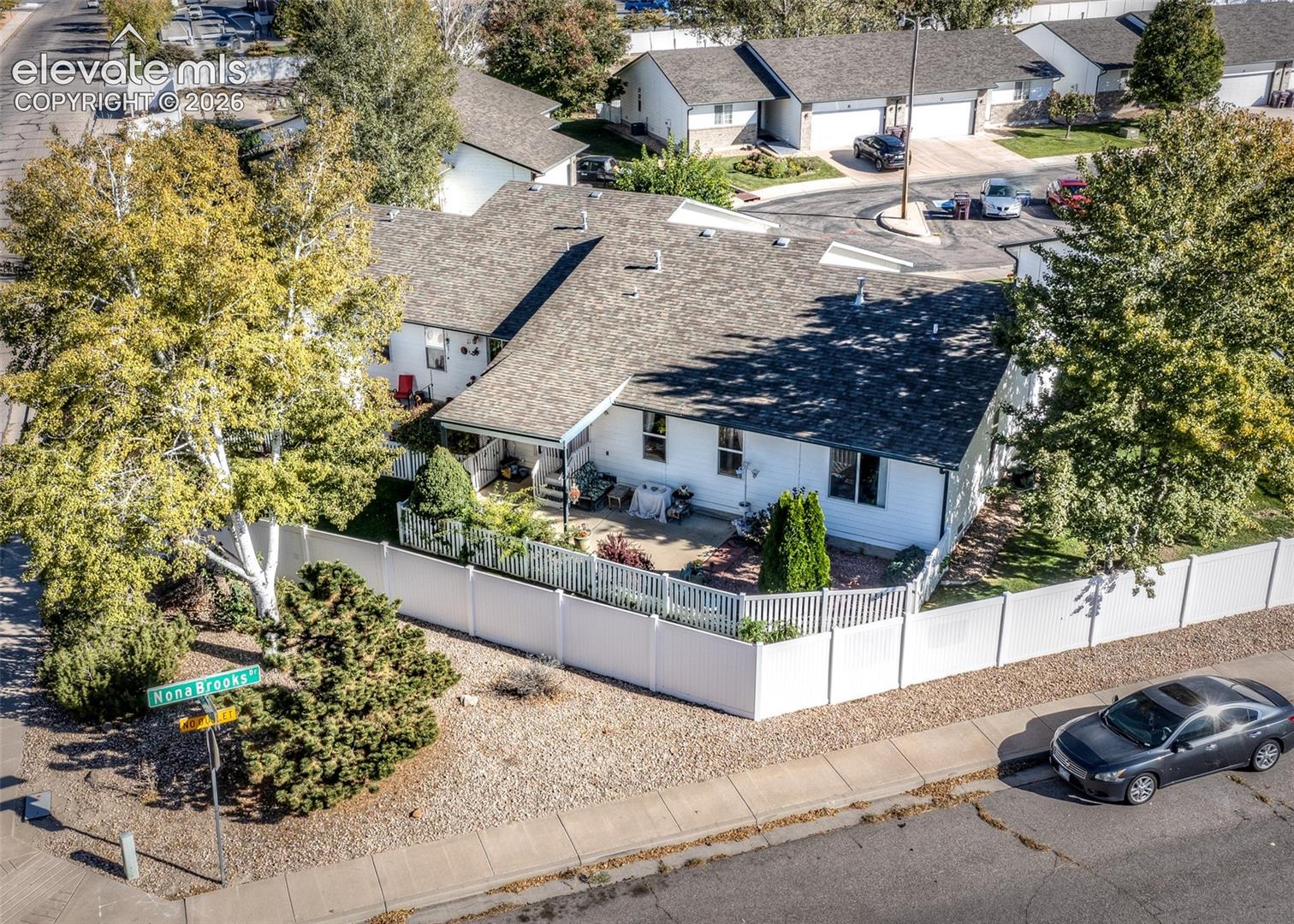 Corner lot residence featuring a white vinyl privacy fence, multi-pitched shingled roof, exterior siding, and a paved patio area