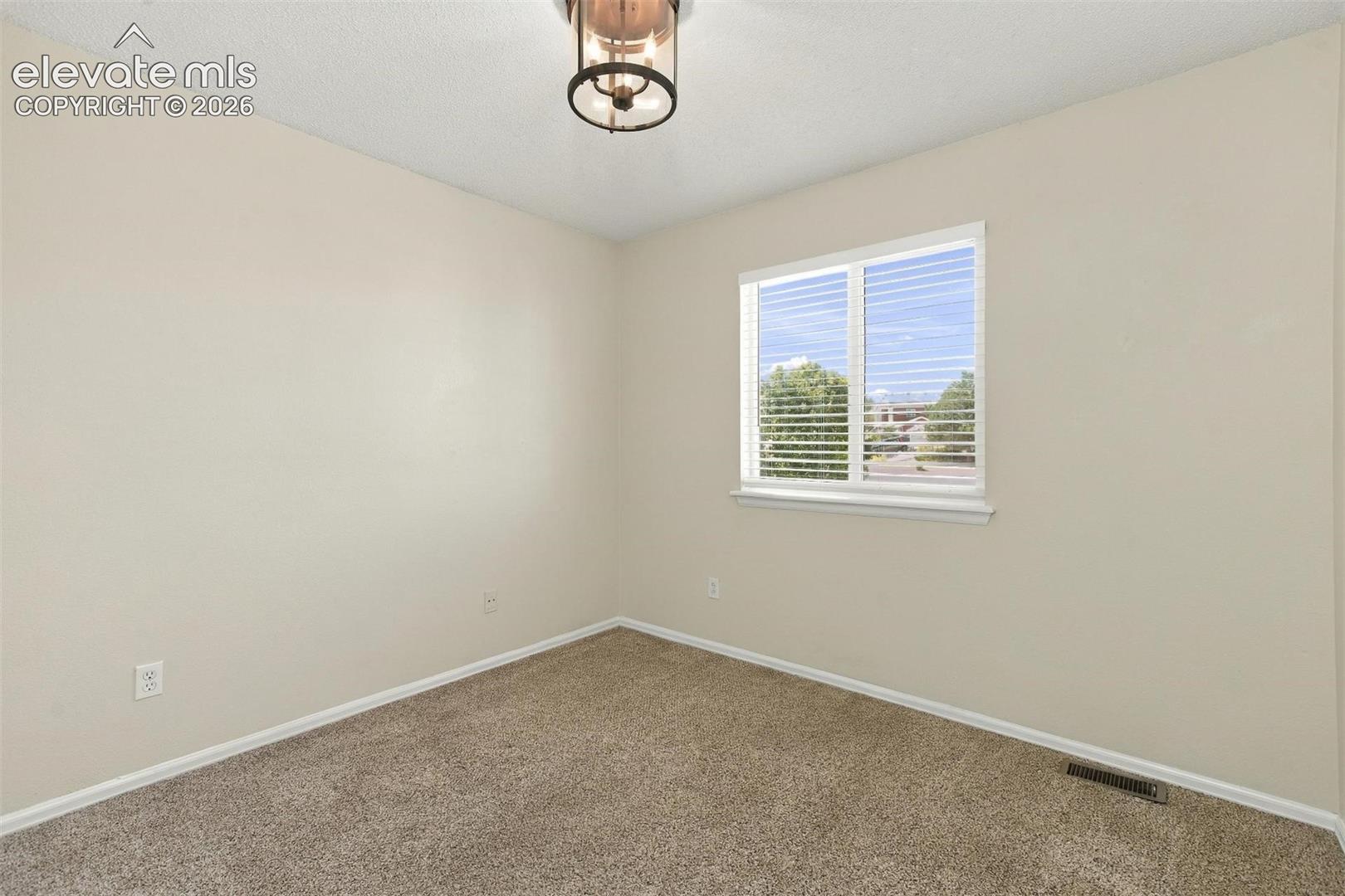 Neutral-toned interior space featuring wall-to-wall carpeting, a single window with blinds, and a drum-style ceiling light fixture