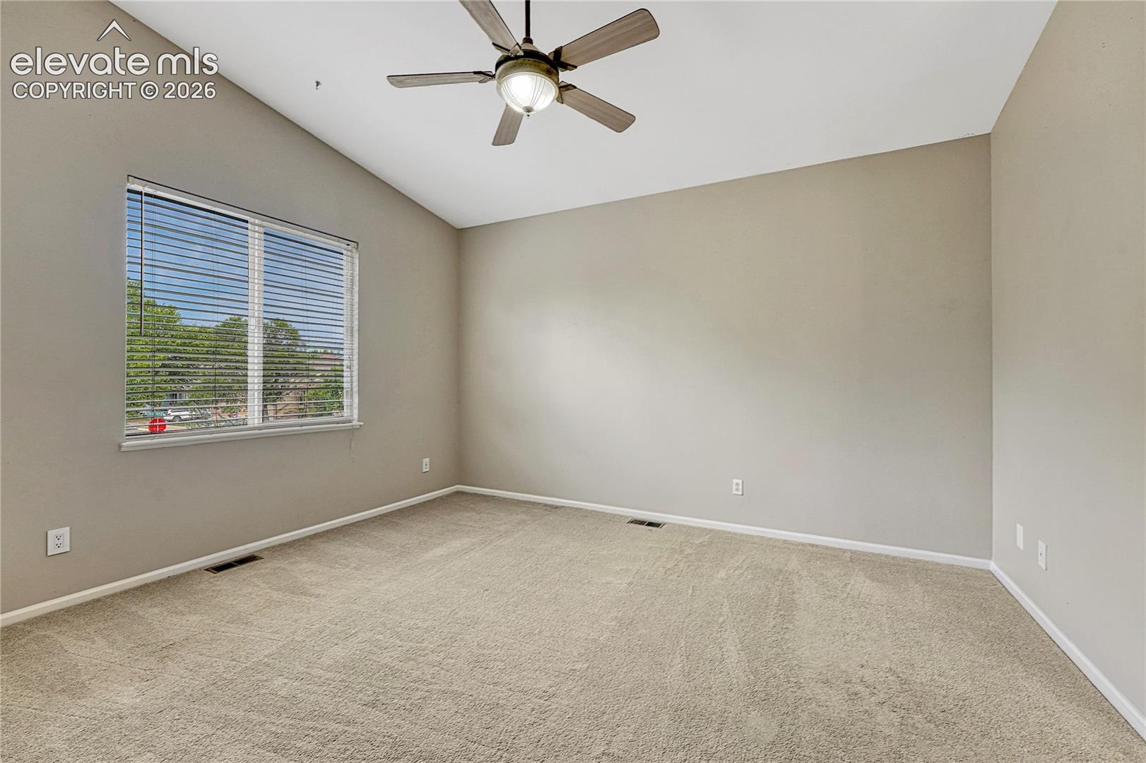 Vaulted ceiling featuring a central multi-blade ceiling fan with integrated lighting, neutral wall finishes, and wall-to-wall carpeting