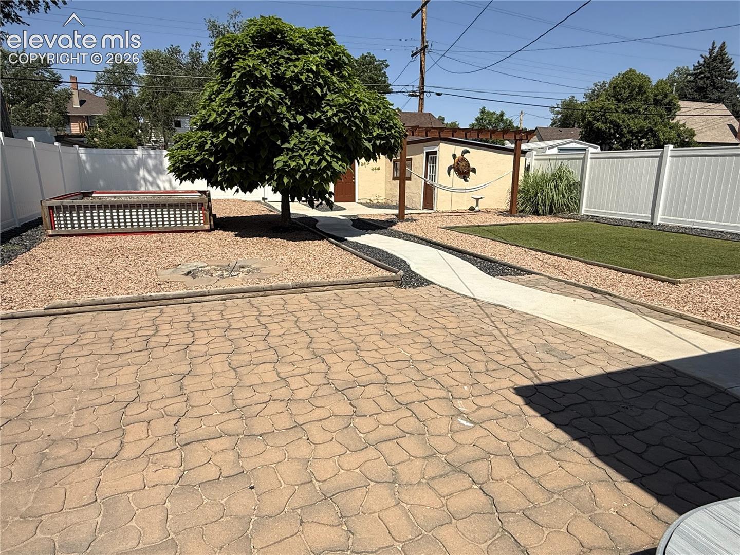Backyard featuring a stamped concrete patio, synthetic turf area, stone-covered landscaping, wood pergola, and white vinyl privacy fencing