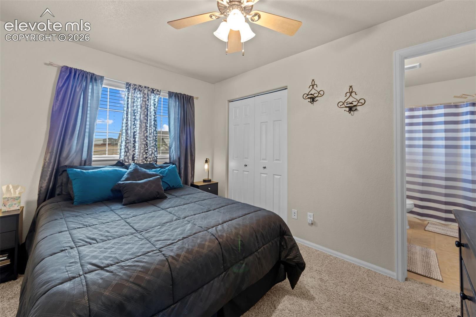 Wall-to-wall carpeting with a ceiling fan light fixture, window with blinds, and white bi-fold closet doors
