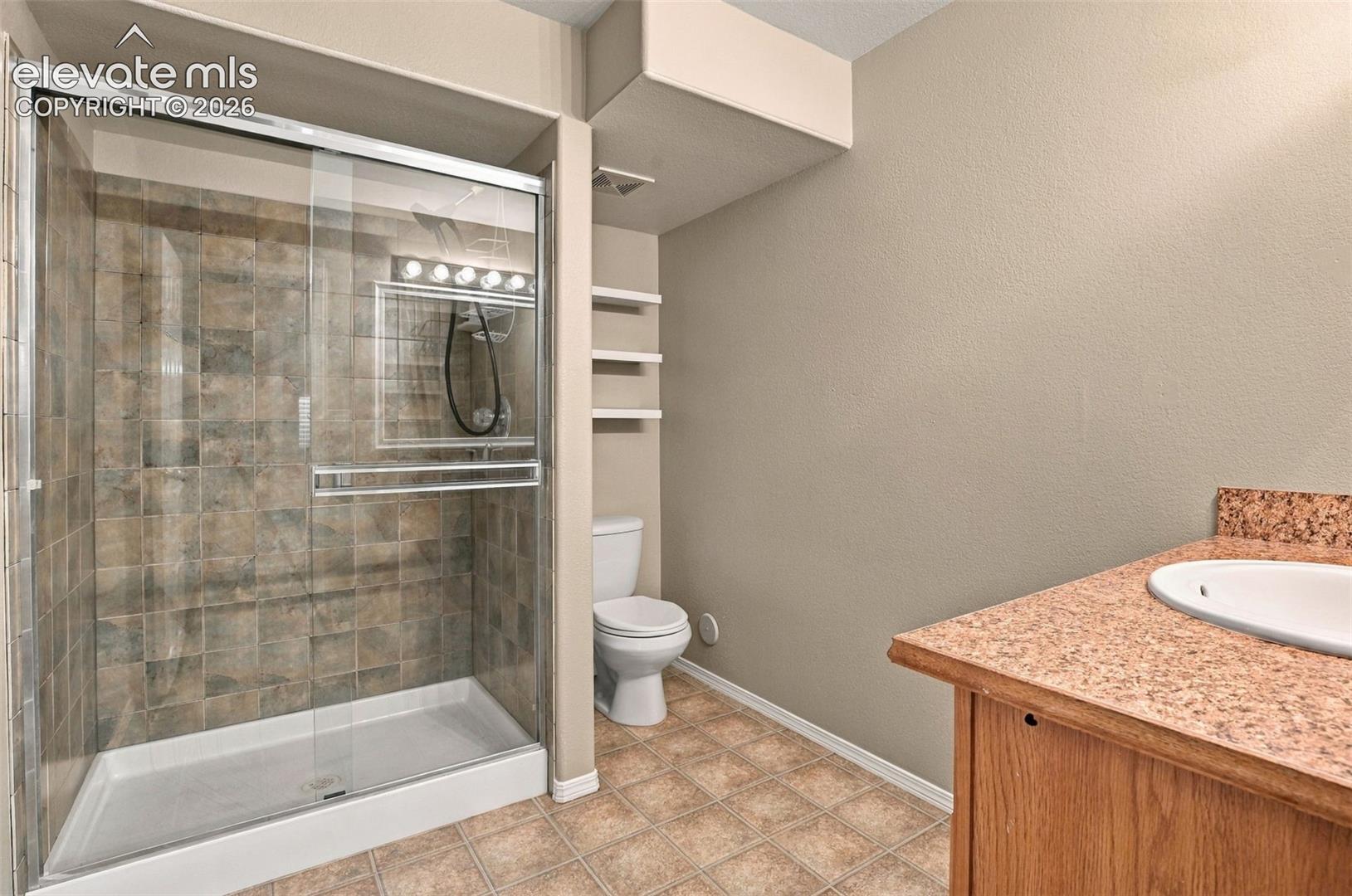 Glass-enclosed shower with tile surround, built-in shelving, wood-finish vanity with an integrated sink, and patterned floor tiling