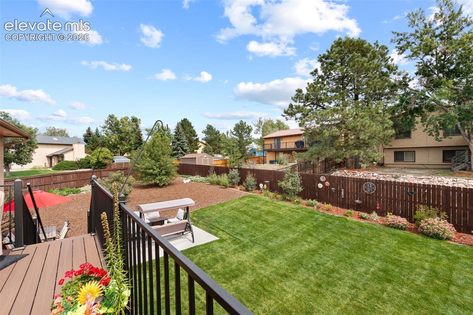 Composite deck featuring black metal railing, manicured lawn, stone-mulched landscaping, concrete patio, and full-perimeter wood fencing