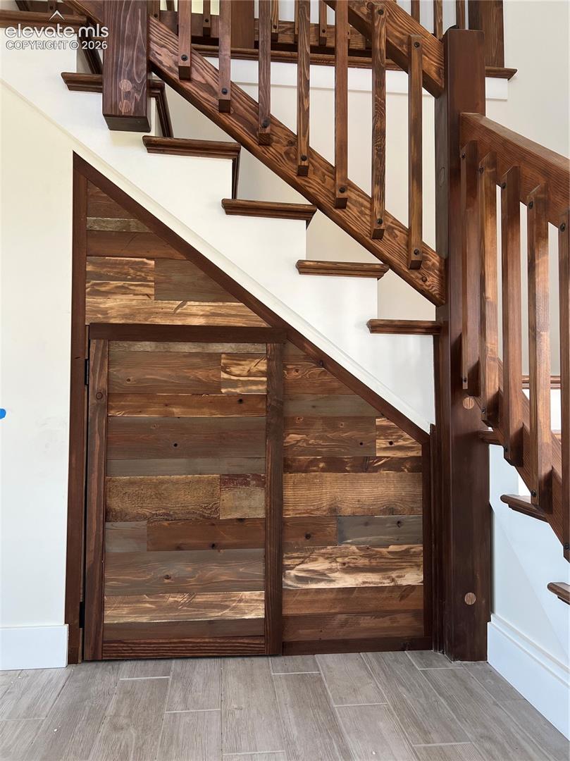 Hardwood staircase with traditional balusters, featuring under-stair storage with rustic wood paneling and a light-colored tile floor