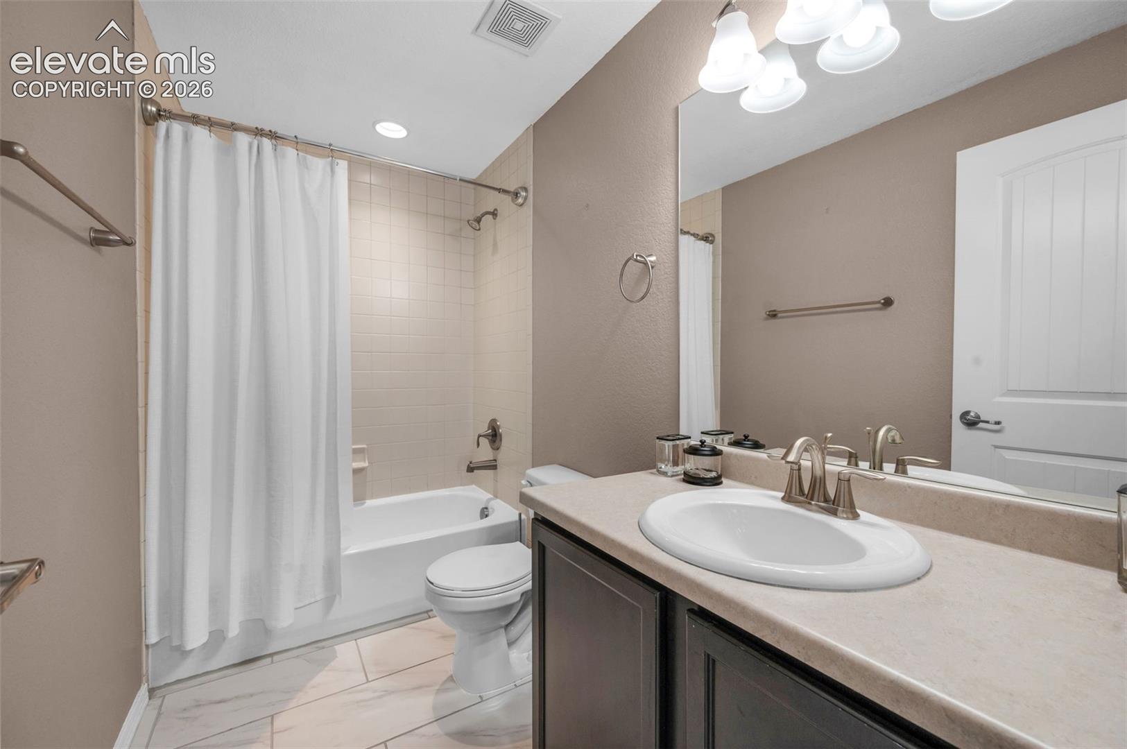 Full bathroom featuring a white bathtub with subway tile surround, brushed nickel fixtures, a dark wood-finish vanity with an integrated sink, a large wall-mounted mirror, and wood-look tile flooring