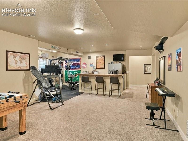 Recessed lighting, wood-finish bar, and carpeted flooring define this versatile space